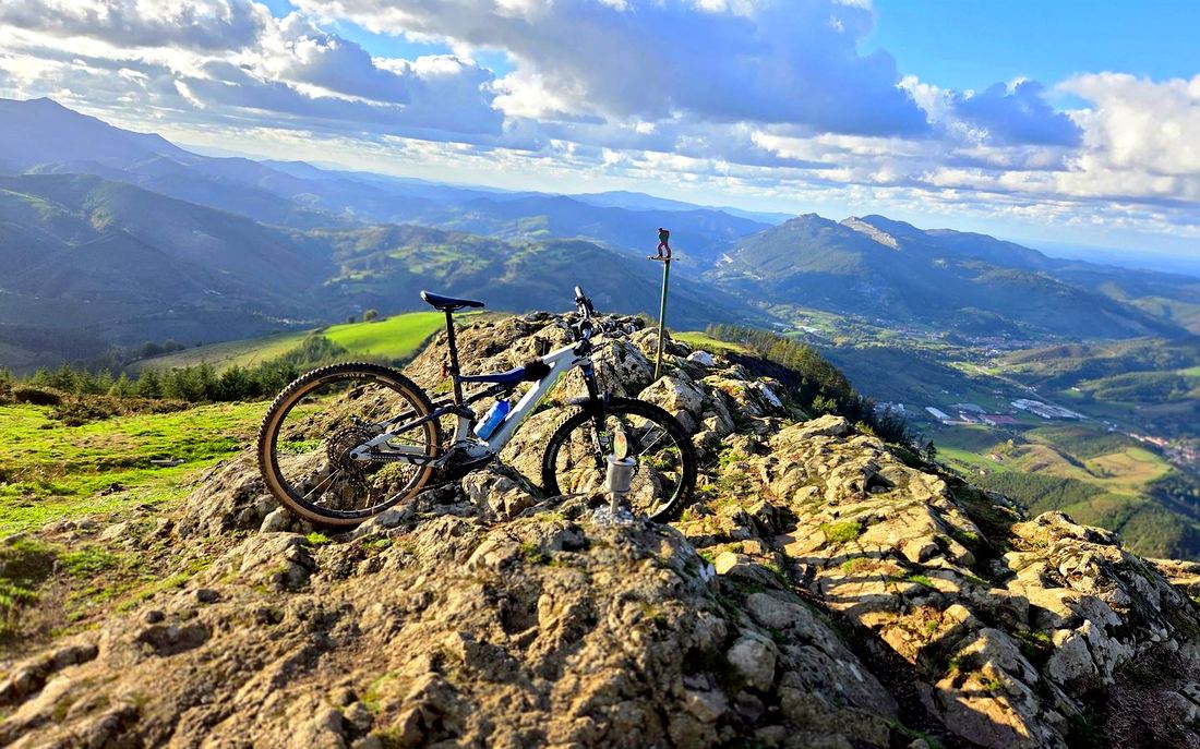 La e-bike apoyada en las rocas de la cima de Kalamua, con los montes y el valle al fondo